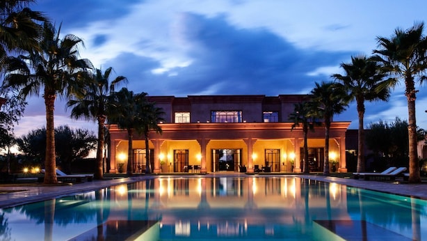 A hotel with a large pool, palm trees, and a well-lit entrance.