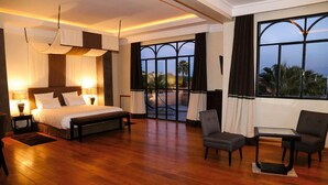 A spacious hotel room with a large bed, a seating area, and a balcony with a view.