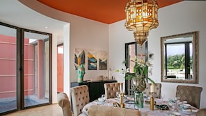 Uma sala de jantar com uma mesa posta para seis pessoas, rodeada por cadeiras estofadas, um vaso decorativo com flores e um espelho grande na parede.