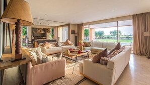 A spacious living room with a large sofa set, a coffee table, and a TV. There is a dining area with chairs and a table, and a kitchen in the background. - Villa Ziram - Four Bedroom Villa, Sleeps 8 (Sidi Youssef Ben Ali)