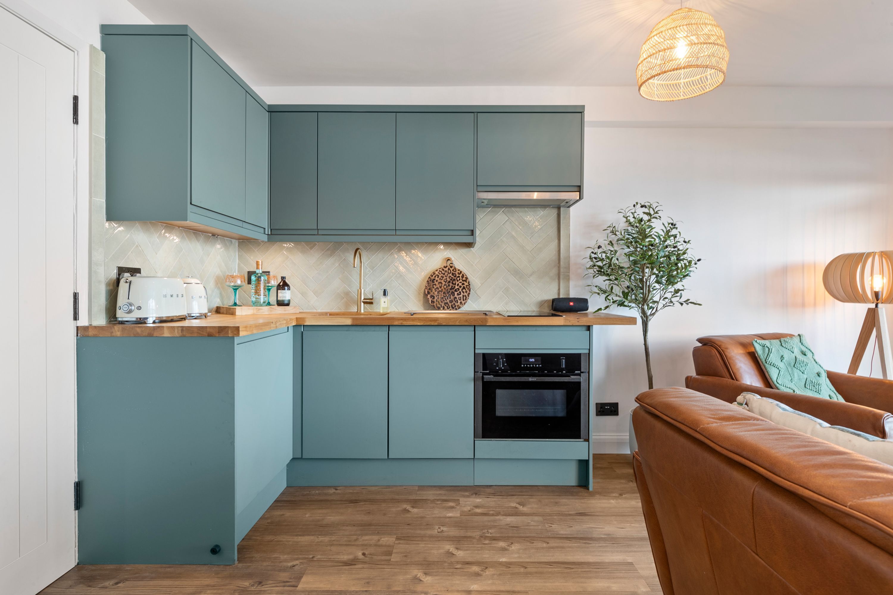 A modern kitchen with teal cabinets, a wooden countertop, and a built-in oven. - Beach Retreat - Sea Views, Parking, Beach Access (Saundersfoot)