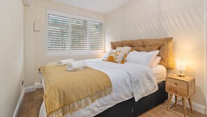 A bedroom with a bed, bedside table, and window with blinds. - Beach Retreat - Sea Views, Parking, Beach Access (Saundersfoot)