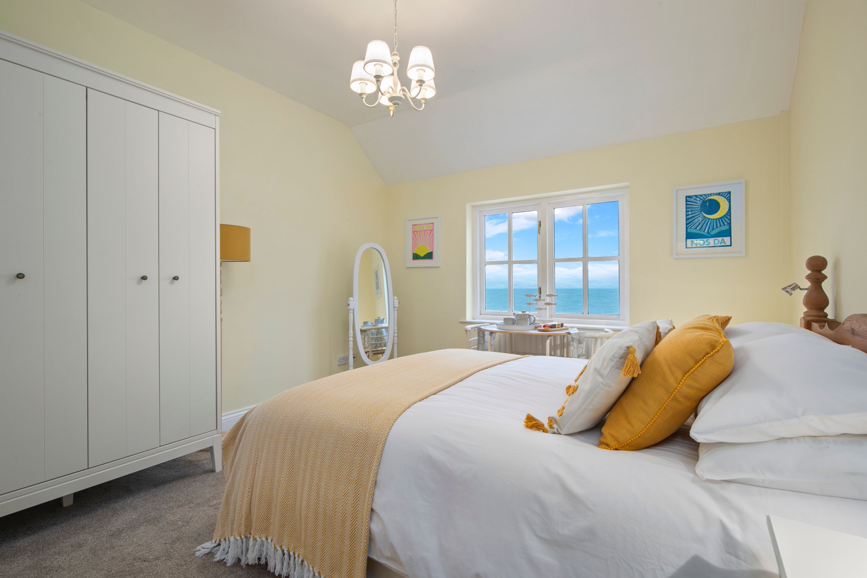 A bedroom with a bed, a wardrobe, a window with a view, a chandelier, and a wall with a picture.
