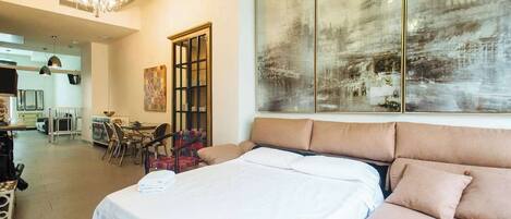 A hotel room with a large bed, a dining area, and a view of a traditional building.
