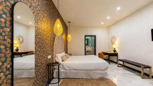 A modern bedroom with a large bed, a sitting area with a desk, and a bathroom visible through an open door. - Argote 1 - Two Bedroom Apartment, Sleeps 4 (Sevilla)