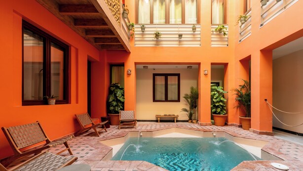 Una piscina amb una terrassa enrajolada, seients de relaxació de fusta i plantes en testos.