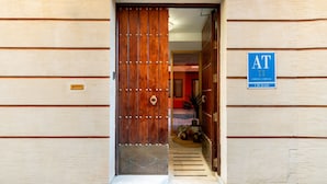 A wooden door with a metal handle and a glass panel, leading into a building with a blue sign reading "AT CIUDAD".