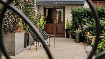 Entrada de un hotel boutique con toldo negro, puerta de madera y plantas en macetas.