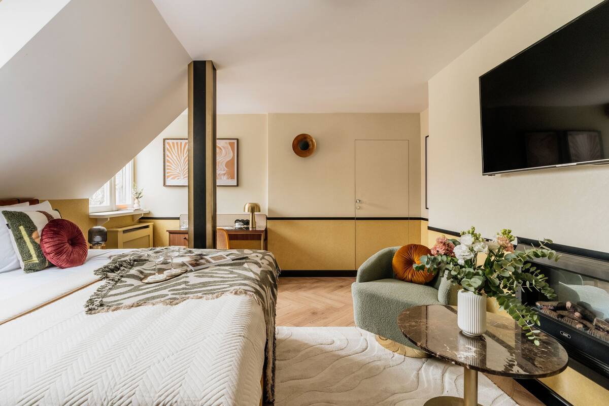 Une chambre moderne avec un grand lit, un coin salon avec une table et un téléviseur fixé au mur.