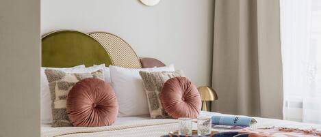 A neatly made bed with a patterned blanket, multiple pillows, and a bedside table with glasses and a book.