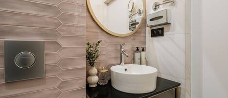 A modern bathroom with a round mirror, a white sink, and a hexagonal tile backsplash.
