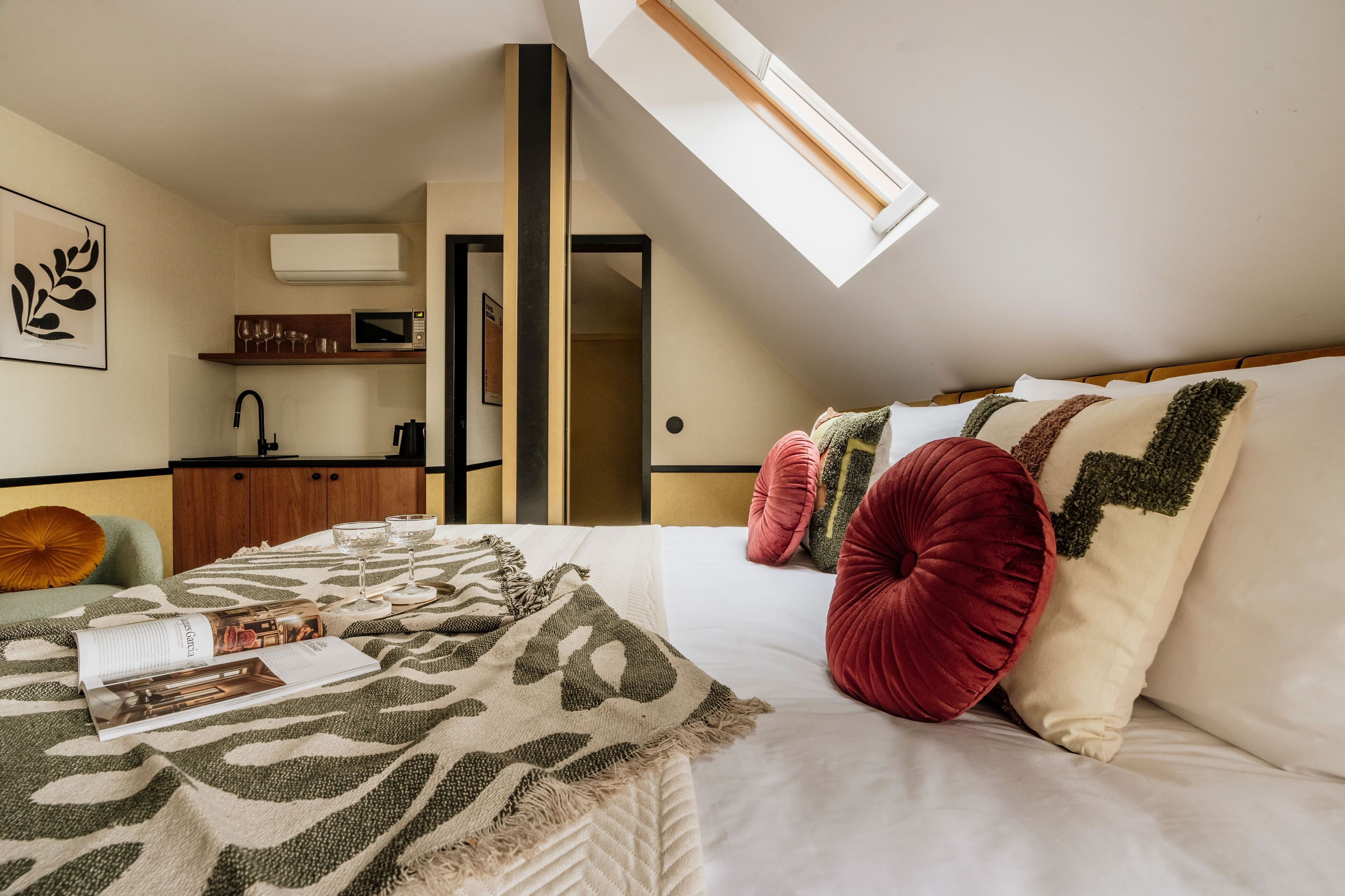 Une chambre à coucher avec un lit, des oreillers, une couverture, un magazine, un four à micro-ondes, un évier et une fenêtre.