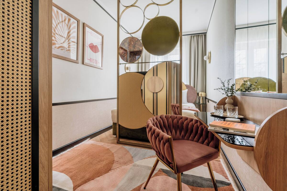 Un intérieur moderne agrémenté d’un fauteuil en velours capitonné, d’une œuvre d’art murale aux motifs géométriques et d’un miroir rond.