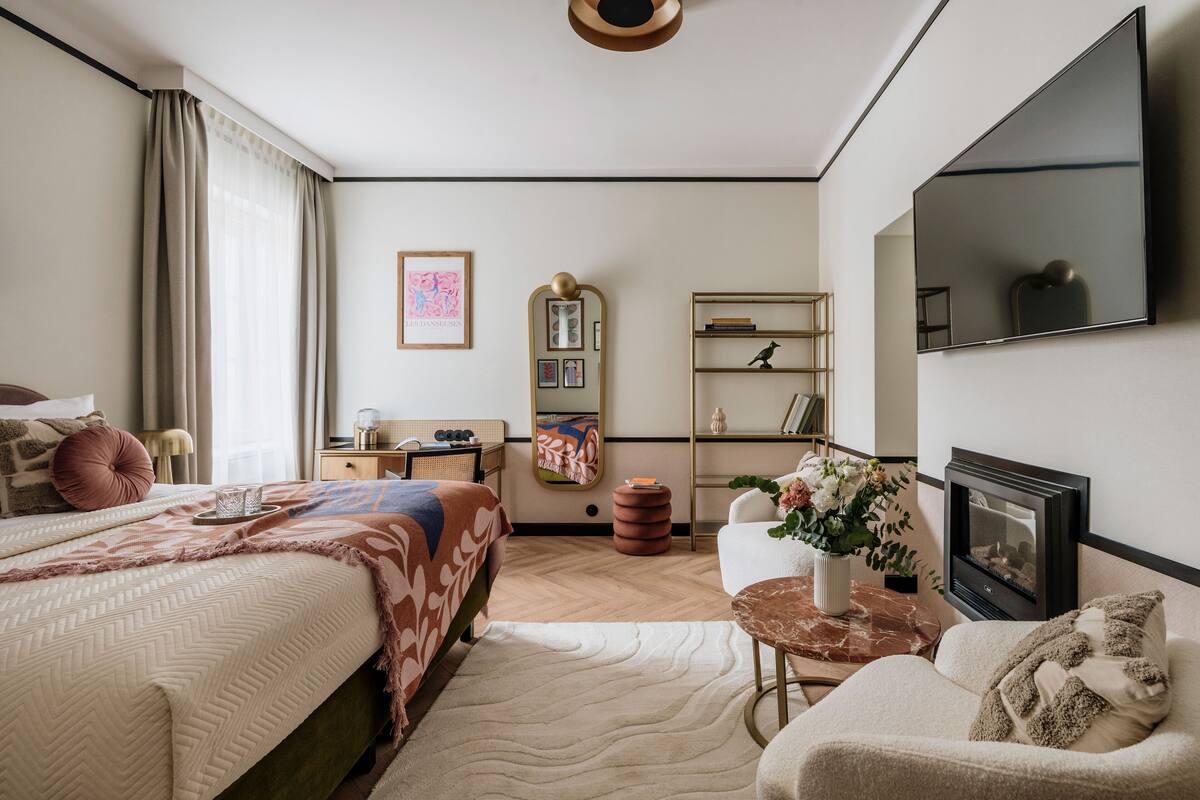 Une chambre d’hôtel comprenant un lit, un canapé, une télévision, une cheminée, une bibliothèque et un miroir.