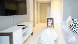 A modern living room with a flat-screen TV mounted on the wall, a white console table, a round coffee table, and a grey sofa with patterned cushions. - Elegant 1B Stunning Views & Balcony Business Bay (Dubai)