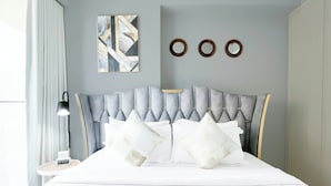 A modern bedroom with a tufted headboard, white bedding, and a bedside table with a lamp. - Elegant 1B Stunning Views & Balcony Business Bay (Dubai)