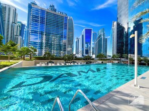 Ein Schwimmbecken mit klarem, blauem Wasser, umgeben von modernen Hochhäusern und Palmen.