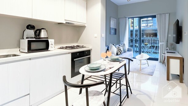 A modern kitchen with white cabinets, a microwave, and a gas stove. There is a dining area with a table, chairs, and a view of the outside balcony. - Elegant 1B Stunning Views & Balcony Business Bay (Dubai)