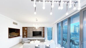 A modern living room with a flat-screen TV, a chandelier, and a dining area with a table set for two. - Elegant 2B at Boulevard Pointburj & Fountain View (Dubai)