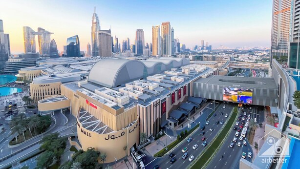 A modern urban landscape with a prominent mall, multiple high-rise buildings, and a busy road network. - Elegant 2B at Boulevard Pointburj & Fountain View (Dubai)