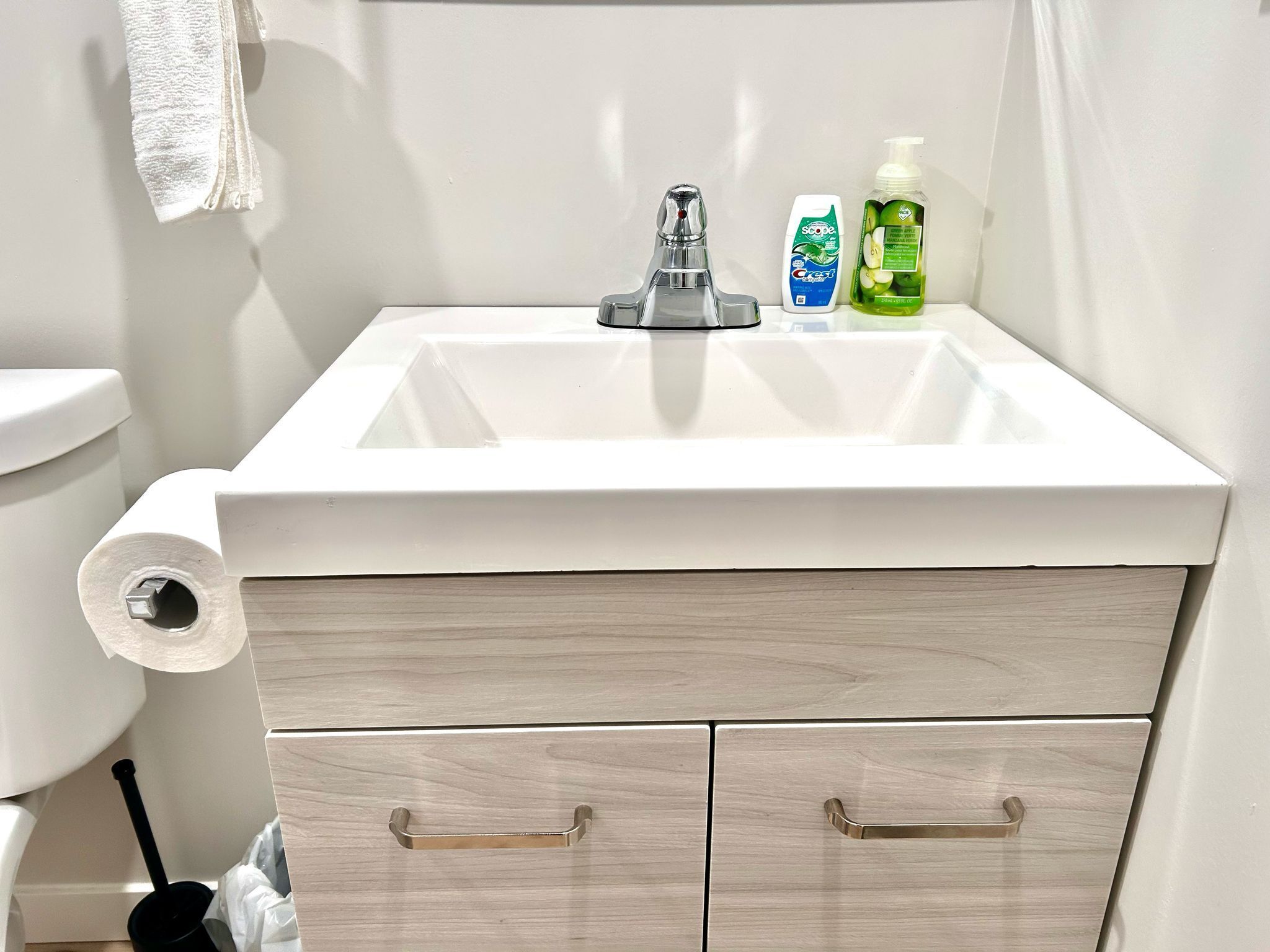 Et badeværelse med en hvid vask, toilet og et håndklæde hængende på væggen.