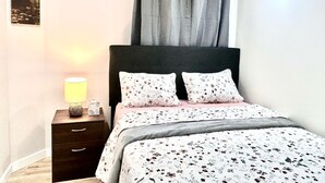 A bedroom with a bed, two pillows, a bedside table with a lamp, and a picture on the wall.