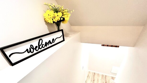 A staircase with a 'welcome' sign and a vase of yellow flowers.