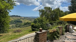 A patio with a yellow umbrella, brick walls, and a view of rolling hills. - Villa Santa Maria (Montegiorgio)