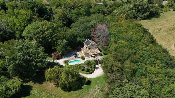 Vista aérea de una casa rodeada de abundante vegetación, con piscina y un camino de acceso a la entrada.