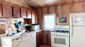 A compact kitchen with wooden paneling, a white stove, a microwave, and a refrigerator. - Brookside Cottages and Resort Freedom Cottage (Grawn)