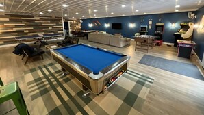 A pool table in a room with a checkered floor, a sofa, and a small table with chairs.