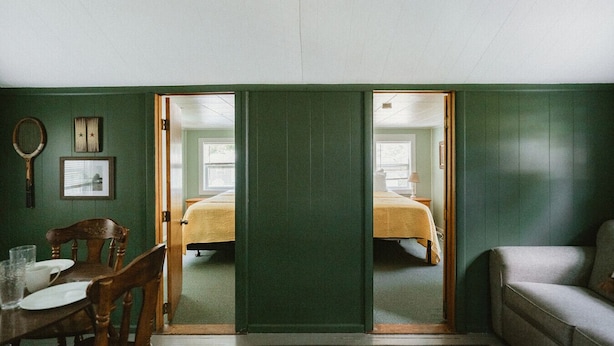 A room with a bed, a chair, a table with a glass, and a couch. - Brookside Cottages and Resort Willow Cottage (Grawn)
