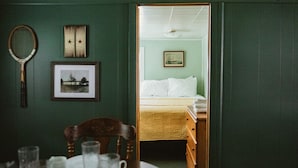 A room with a bed, a framed picture, a tennis racket, and a wooden chair. - Brookside Cottages and Resort Willow Cottage (Grawn)