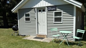 A small, single-story building with a white exterior and a 'Fayes' sign above the door. There is a grill and two green folding chairs outside.