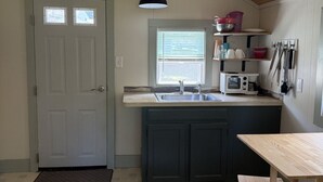 A kitchen with a wooden ceiling, a double door, a window, a sink, a microwave, and a small dining area.
