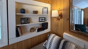 A cozy room with wooden paneling, a white shelf with books and decorative items, a lamp, and a mirror reflecting the room. - Brookside Cottages and Resort Brookside Cottage (Grawn)
