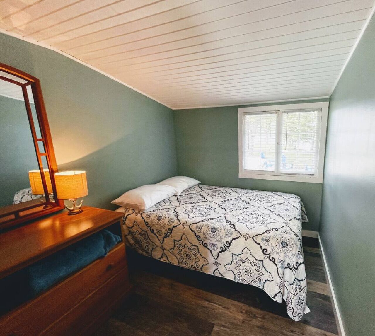 Une chambre à coucher avec un lit, une commode, un miroir et une fenêtre.