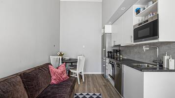 Una cocina compacta con comedor, un sofá marrón con un cojín rosa y una pequeña mesa con sillas.