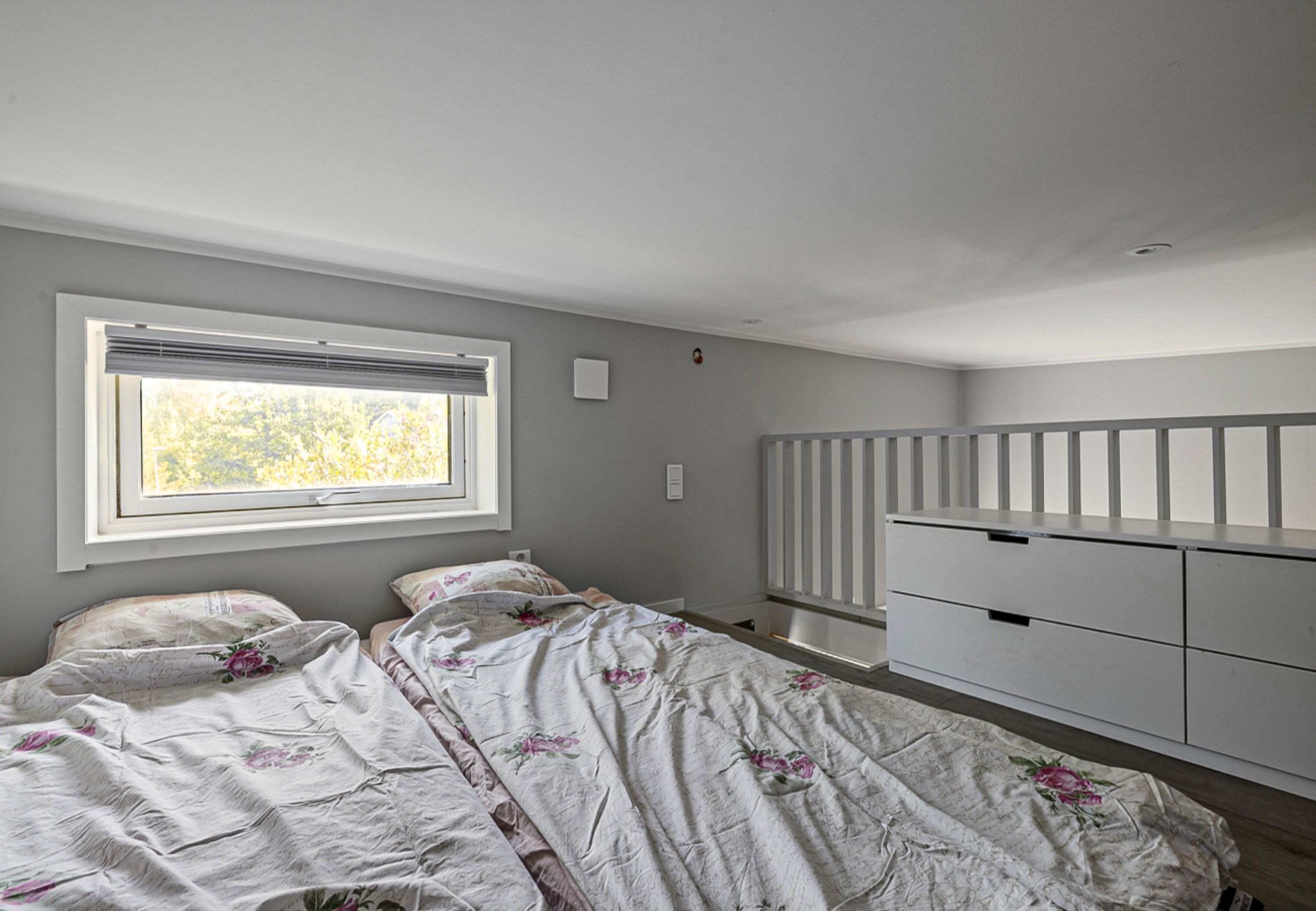 A bedroom with two beds, a window, a white dresser, and a radiator.