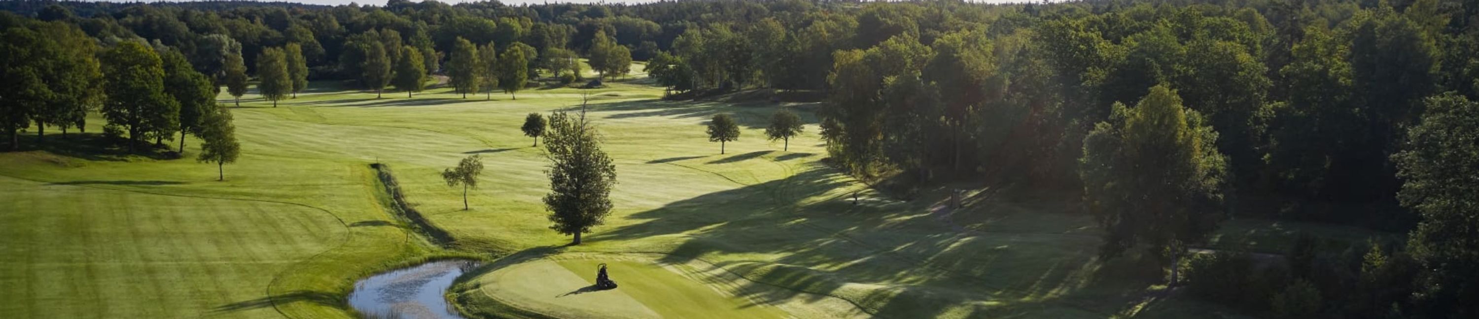 Un campo de golf con un obstáculo acuático, árboles y cielo despejado.