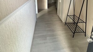 A narrow hallway with beige walls and a wooden floor. There is a black metal rack with hangers on the right side. - Cozy vacation apartment directly at the highway entrance (Freudenberg)