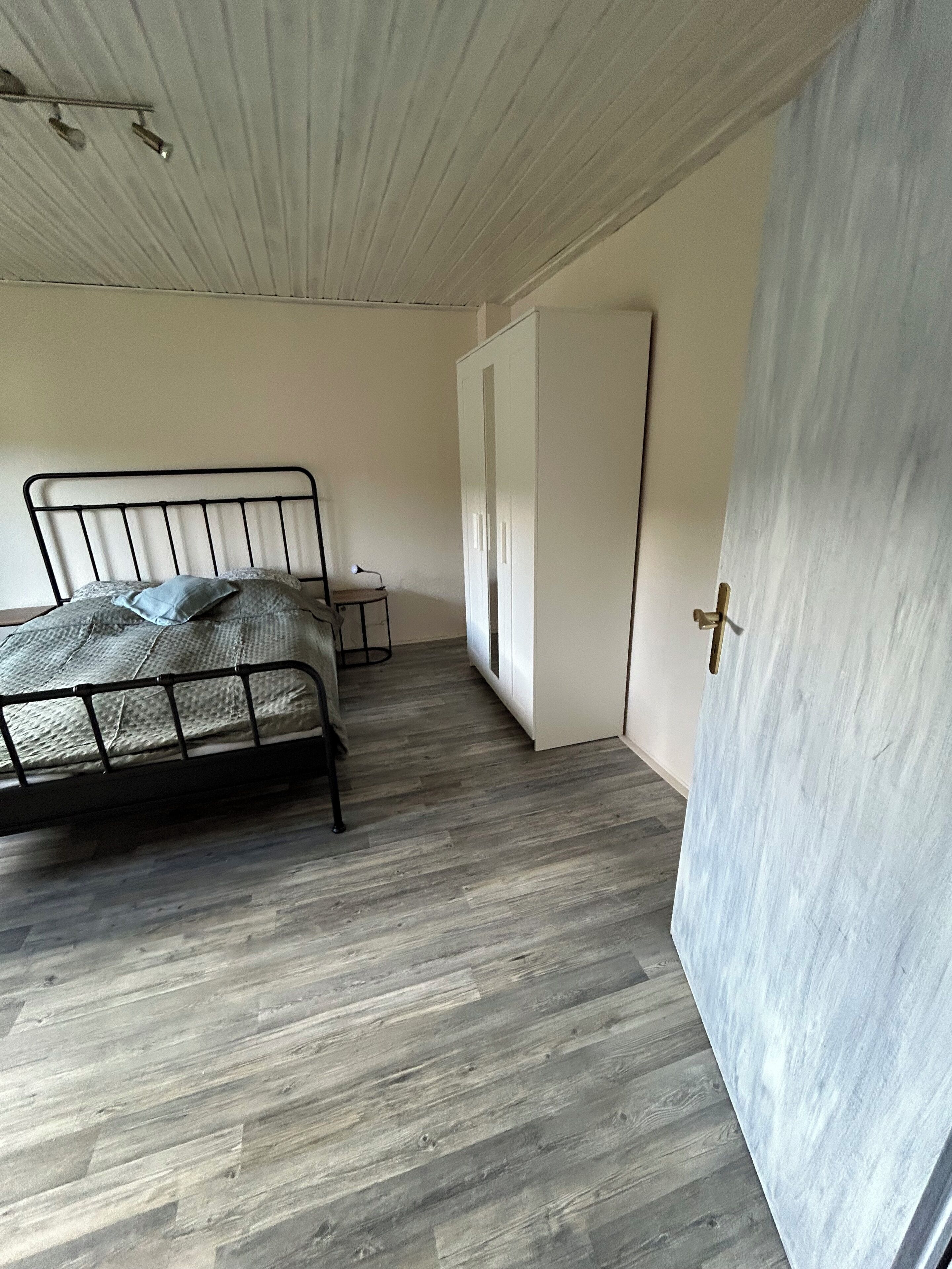 Ein Schlafzimmer mit einem Metallbettgestell, einem kleinen Nachttisch und einem Kleiderschrank.