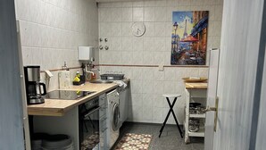 A compact kitchen with a washing machine, a coffee maker, and a small dining area with a painting of a Parisian street scene. - Cozy vacation apartment directly at the highway entrance (Freudenberg)