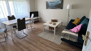 A living room with a dining area, a TV, a painting on the wall, and a lamp. - Cozy vacation apartment directly at the highway entrance (Freudenberg)