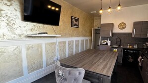 Une cuisine moderne avec un îlot central en bois, un téléviseur à écran plat fixé au mur et des luminaires suspendus.