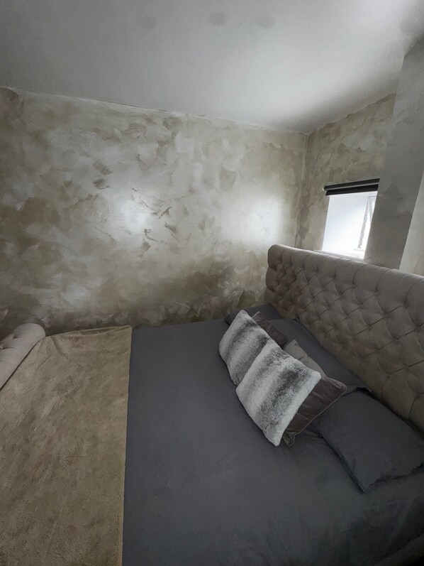 A bedroom with a bed, a window, and a wall with visible damage.