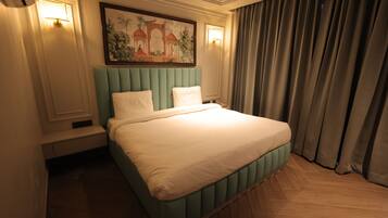 A hotel room with a large bed, a headboard with vertical panels, a wall-mounted painting, and a window with curtains.