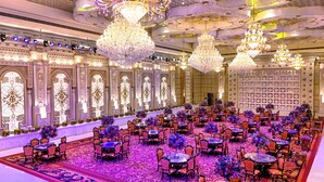 Un salón de baile majestuoso con candelabros ornamentados, mesas y sillas dispuestas para un evento formal.
