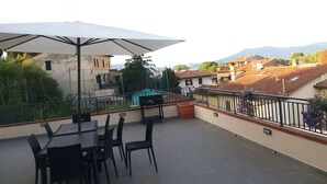 A terrace with a table and chairs, an umbrella, and a view of buildings and mountains. - 01. Apartment (Signa)