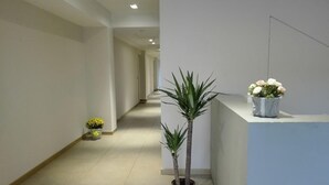 A hallway with a reception desk, potted plants, and a tiled floor. - 01. Apartment (Signa)